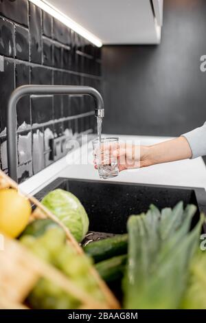 Frau füllt Trinkglas mit Leitungswasser in der Küche. Konzept des sauberen Trinkwasserhahns zu Hause Stockfoto