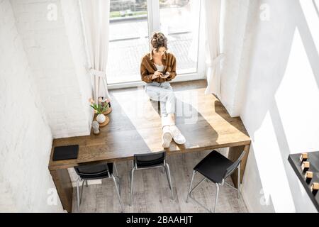 Frau sitzt mit Telefon auf der riesigen Fensterbank zu Hause, Blick von oben Stockfoto