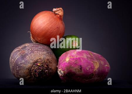 Haufen aus roten Beeten, Avocado und Rosenkartoffeln Obst und Gemüse mit einer orangefarbenen Zwiebel oben vor dunklem Hintergrund Stockfoto