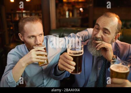 Zwei Männer halten Brille in den Händen und genießen das Bier, während sie in der Bar sitzen Stockfoto