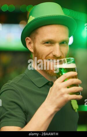 Porträt des jungen Mannes mit rotem Bart, der Bier trinkt und beim stehen in der Kneipe mit der Kamera lächelt Stockfoto