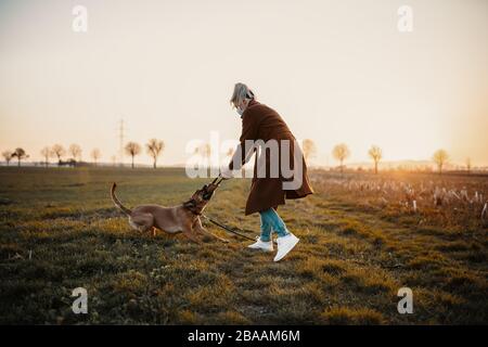 Frau, die eine Schutzmaske trägt, geht allein mit einem Hund im Freien wegen der Corona-Virus-Pandemie Kovid-19 Stockfoto