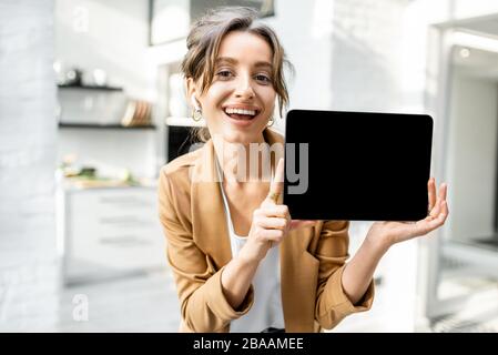 Gut gekleidete, fröhliche Geschäftsfrau mit einem digitalen Tablet in Innenräumen, das Tablet mit schwarzem Bildschirm zum Kopieren von Paste zeigt Stockfoto