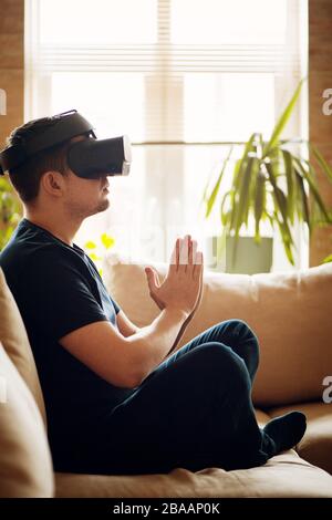 Junger Mann meditiert auf Sofa in VR-Brille. Neues Technologiekonzept. Stockfoto