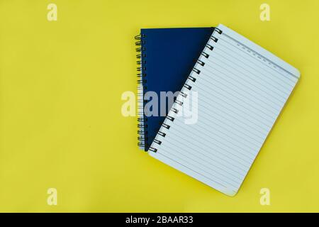 Zwei blaue Notizbücher übereinander über einem gelben Papierhintergrund Stockfoto