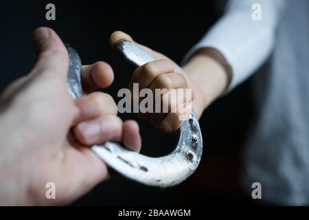 Sicht auf die kaukasische männliche Hand, die einem Kind mit weißem Hemd einen glänzenden polierten Horschuh aus Stahl in natürlichem Licht gibt Stockfoto