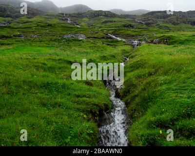Die Färöer sind das Land der Wasserfälle, die grüne Felder durchschnitten und in den Ozean fallen. Stockfoto