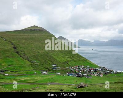 Faröer Inseln, Eysturoy, Funnings Kommune. Blick auf die Stadt im Tal. Es ist umgeben von grünen Feldern, grünen Bergen und Meer. Stockfoto