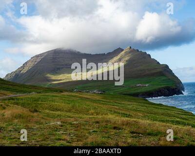 Viðoy, Viðareiði,  . Spektakulärer Blick auf Klippen und grüne Hügel über dem Dorf. Blauer Himmel mit einigen Wolken. Stockfoto