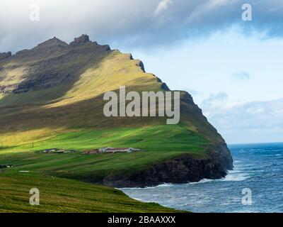 Viðoy, Viðareiði,  . Spektakulärer Blick auf Klippen und grüne Hügel über dem Dorf. Blauer Himmel mit einigen Wolken. Stockfoto