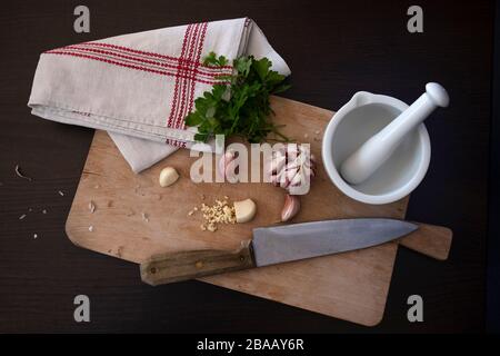 Knoblauchzehe auf einem Schneidebrett mit einem Messer und einem alten Geschirrtuch Stockfoto