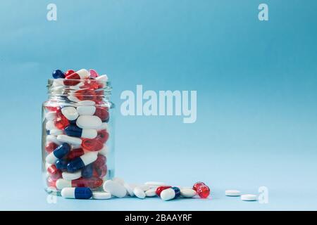 Ein medizinisches Konzept eines Gefäßes voller Drogen, Tabletten und Pillen auf blauem Hintergrund mit Kopierraum. Stockfoto