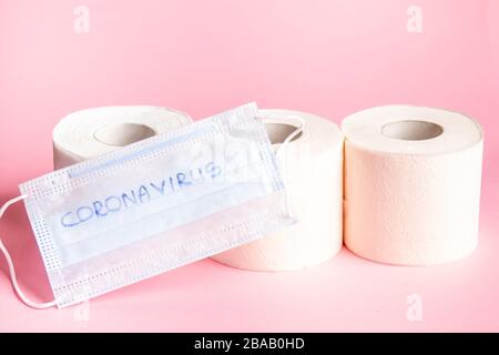 Drei Rollen weißes toilettenpapier auf pinkfarbenem Hintergrund mit einer medizinischen Einwegmaske Stockfoto