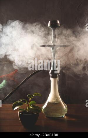 Rauch aus einer Kapuze in einer Bar auf einem Tisch auf dunklem Hintergrund. Rauchen für Entspannung. Stockfoto