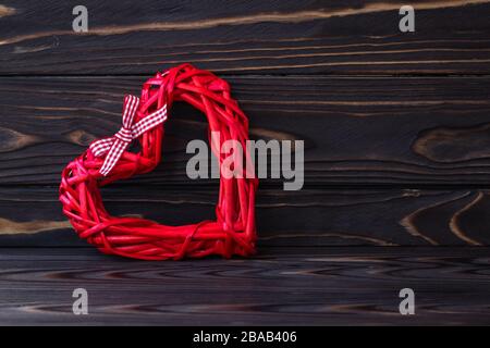 Rotes Herz auf dunklem Holzhintergrund. Braune Bretter Textur. Geschenkgutschein für Valentinstag. Symbol der Liebe, romantisches Konzept. Feiertagsrahmen im lakonischen Stil, Stockfoto