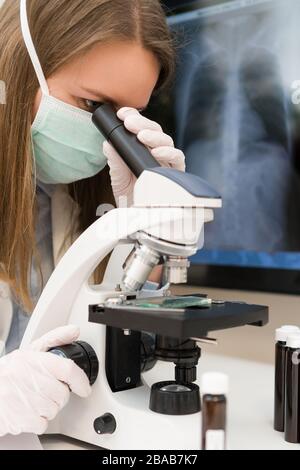 Wissenschaftler in der medizinischen Maske im Labor. Röntgenfilm mit Lungenentzündung im Hintergrund. Stockfoto