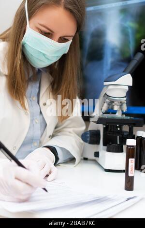 Wissenschaftler in der medizinischen Maske im Labor. Röntgenfilm mit Lungenentzündung im Hintergrund. Stockfoto