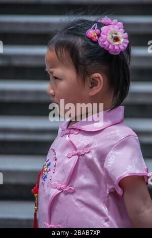 Shanghai, China - 4. Mai 2010: Nahaufnahme des jungen Mädchens in rosafarbenem Kleid und Haarspeld mit grauen Stufen im Rücken. Stockfoto