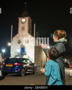 20:00 Uhr 20:00 Uhr, Großbritannien. März 2020. Lauder, schottische Grenzer, die heute Abend in einem Sperrgebiet über Großbritannien standen, öffnete Fenster und stand in Türen, um zu klatschen und Lärm zu machen, um die Mitarbeiter des nationalen Gesundheitsdienstes NHS zu unterstützen und ihnen Dank zu senden, die dem Kampf gegen die Pandemie COVID-19, Coronavirus, die die Welt überschwemmt hat, helfen. PIC zeigt den kleinen Jungen und seine Mutter vor der Haustür, die im Hintergrund mit der Lauder Uhr und dem Rathaus klatschen. Credit: phil wilkinson/Alamy Live News Stockfoto