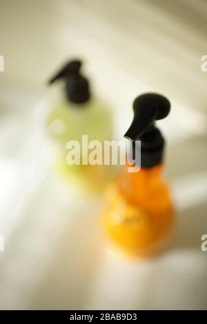 Orange- und kalkgrüne Flaschen mit schwarzen Dispenser auf einem weißen Tisch, schöner selektiver Fokus. Stockfoto