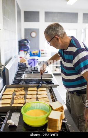 Älterer Mann, der in der Industrieküche French Toast kocht. Stockfoto