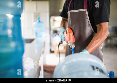 Der Arbeiter spült mit einer Bohrmaschine einen Trinkwasserkrug zur Wiederverwendung aus. Stockfoto