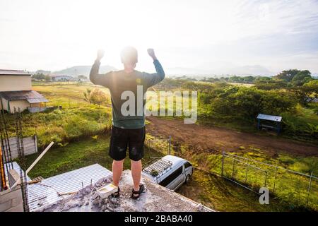 Mann, der Gott von der Dachterrasse bei Sonnenaufgang preist. Stockfoto