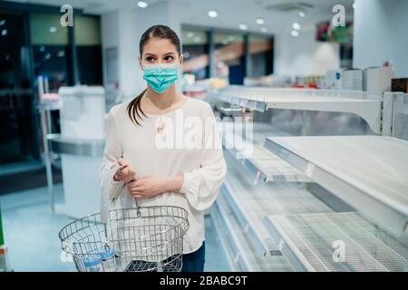 Frau trägt Gesichtsmaske, die in einem Supermarkt/Drogerie mit ausverkauftem Zubehör kauft.Leere Regale im Supermarktgeschäft aufgrund des neuartigen Coronavirus Covid-1 Stockfoto