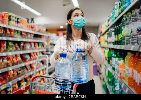 Frau, die Gesichtsmaske trägt, die Wasser in Flaschen im Supermarkt/Drogerie mit ausverkauften Vorräten kauft.Prepper kauft wegen Covid-19 Großbedarf Stockfoto