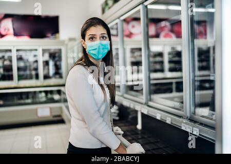 Frau mit Maske und Handschuhen kauft Lebensmittel/Verbrauchsmaterial im Supermarkt mit ausverkauften Produkten.Lebensmittelmangel.Leere Regale wegen neuartiger Korona Stockfoto