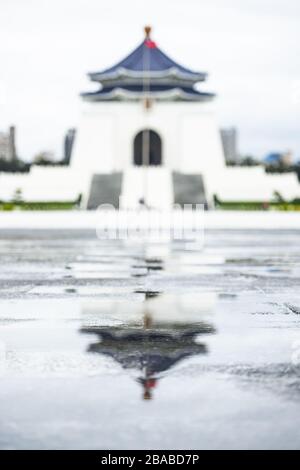 Atemberaubender Blick auf die unscharfe National Chiang Kai-Schek Memorial Hall in der Ferne mit ihrer Spiegelung in einer Pfütze im Vordergrund. Stockfoto
