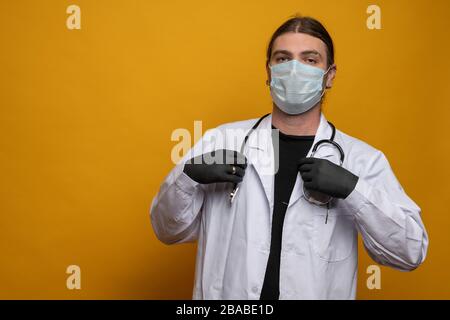 Doktor mit Stethoskop, Schutzmaske trägt seinen Trauring über den dunklen Handschuhen. Vor orangefarbenem Hintergrund aufgenommen. Es wird versucht, sicher vor sa zu bleiben Stockfoto