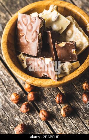 Dunkle und weiße Nussschokolade in Holzschüssel. Gebrochener Schokoladenriegel. Stockfoto