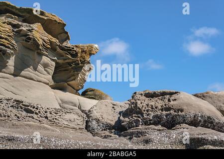 Blick auf die Spitze eines braunen, stark strukturierten, erodierten Sandsteinfiffs, das oben im Vordergrund aufsteigt, mit einem leuchtend blauen Himmel dahinter. Stockfoto