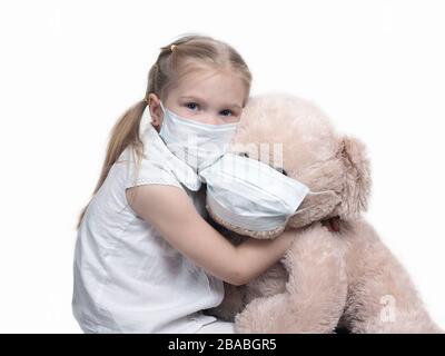 Ein Kind in einer medizinischen Maske umarmt einen großen Spielzeugbären. Stockfoto