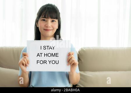 Asian Woman mit einem Blatt Papier mit Text Ich bleibe zu Hause, damit Sie medizinisches Personal anfeuern, um Virus zu schützen und sich um ihre Gesundheit von COVID-1 zu kümmern Stockfoto