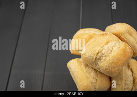 Haufen frisch gebackenes und goldenes Brot bereit zum Verzehr auf grauem Holztisch mit leichten Spuren von Mehl Stockfoto