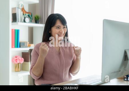 Schöne asiatische Geschäftsfrau arbeitet von zu Hause aus und feiert mit Computer, Erfolg fröhliche Pose. E-Commerce, Hochschulbildung, Internet-Technologie, Stockfoto