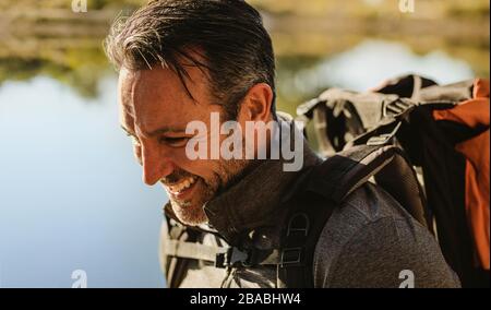 Nahaufnahme eines reifen Mannes mit lächelndem Rucksack. Wohnmobil am See. Stockfoto