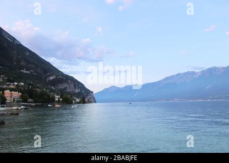 Malerischer Blick gegen die hellen Sonnenstrahlen oberhalb der Felsen im Sicherungskasten Motor Schiff schwimmt auf wunderschönen Gardasee, Lombardei, Italien umgeben von hohen Dol Stockfoto