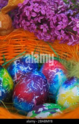 Osterhintergrund. Kunst malte Eier mit Flieder und Feder im Korb. Muster von Kunst und Farben auf Eiern. Stockfoto