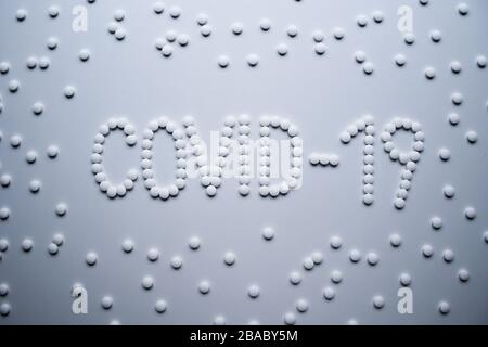 Textphrase Covid-19 Zeichenkonzept aus weißen Pillen auf weißem Hintergrund Stockfoto