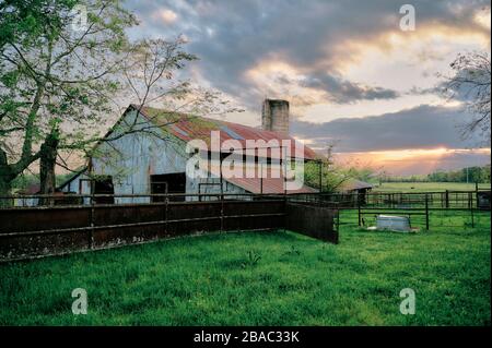 Ländliche amerikanische Küche, Alabama, Bauernscheune bei Sonnenuntergang mit Sonnenstrahlen, die durch Wolken im ländlichen Alabama, USA, kommen. Stockfoto