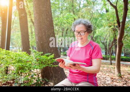 asiatische Seniorin in Brille und Lesebuch im Park Stockfoto