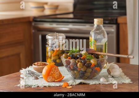 Zubereitung von Olivenöl marinierte schwarze und grüne Oliven mit Gewürzen in der Küche. Stockfoto