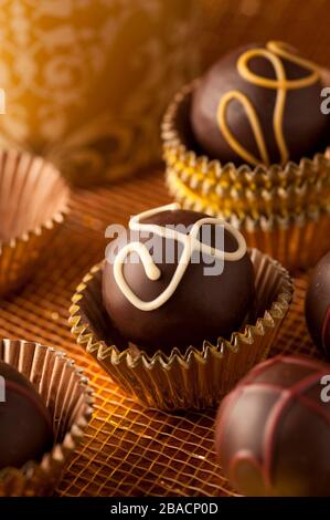 Dunkle Schokoladentrüffel in Goldbecher mit goldenem Hintergrund im Studio gedreht. Stockfoto