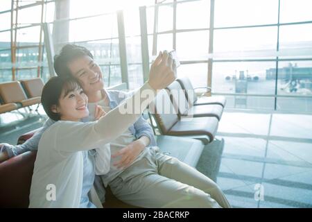 Junge Liebhaber sitzen in der Lounge am Flughafen, um ein Handy zu sehen Stockfoto