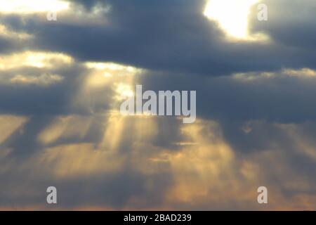 Die Sonne scheint bei Sonnenuntergang oder im Morgengrauen hinter den Wolken durch. Die Strahlen der Sonne am Himmel. Stockfoto