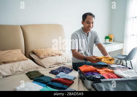 asian man legt seine Kleidung in den Koffer, bevor er in den Urlaub geht Stockfoto