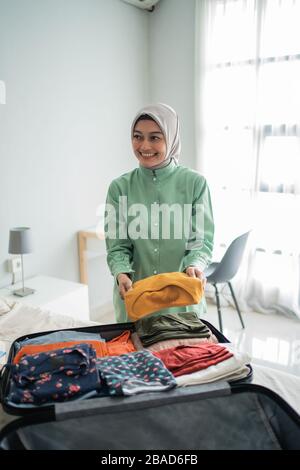 Schöne muslimische Frauen, die sich vor einer Urlaubsreise Kleidung zubereiten, um in einen Koffer gesteckt zu werden Stockfoto